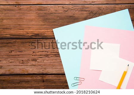 Wooden desk table with a set of supplies, sheets of colored paper, pencil,  paper clips. Top view, empty space for text. 