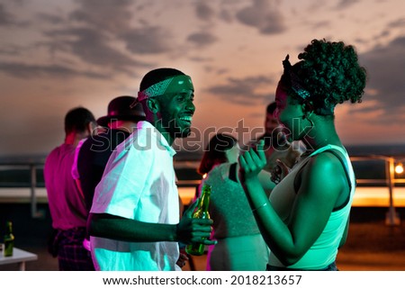 Happy young African couple dancing against their friends at rooftop party Royalty-Free Stock Photo #2018213657
