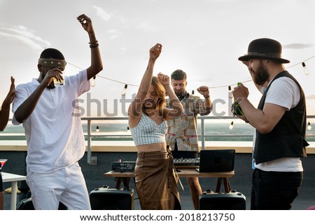 Young intercultural friends and happy deejay dancing together at rooftop party