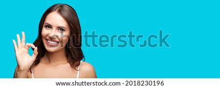 Photo of woman showing ok okay hand sign or zero gesture, isolated on aqua blue green color background. Portrait of happy smiling gesturing brunette girl at studio. Wide horizontal banner composition.