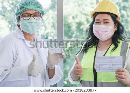 Worker woman and nurse showing Covid 19 vaccination record card after injecting vaccine to get immunity for protect virus. Vaccination for Essential Workers in clinic at industrial factory.