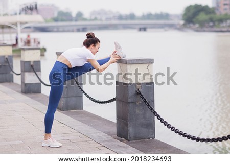 Runner stretching muscles outdoor at summer morning in city. Running athlete woman doing fitness stretch. Healthy young caucasian woman warming up outdoors before exercise.