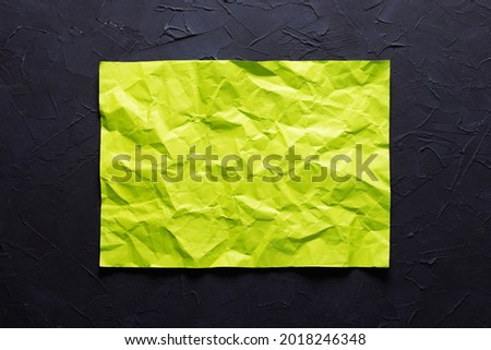 Light green wrinkled or crumpled paper at black abstract background texture