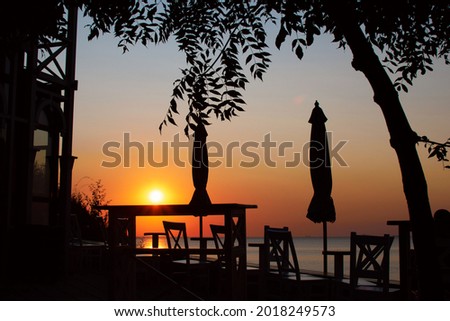 Silhouette of empty street cafe or restaurant against background of beautiful sunrise or sunset over the ocean or sea