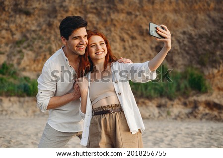 Young couple two friends family man woman in white clothes hug rest together do selfie shot mobile cell phone post photo social network at sunrise over sea sand beach outdoor seaside in summer day.