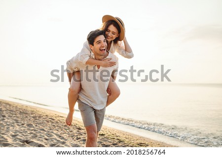 Young excited couple two friends family man woman in casual clothes boyfriend give piggyback ride to joyful girlfriend sit on back at sunrise over sea beach ocean outdoor seaside in summer day evening Royalty-Free Stock Photo #2018256764