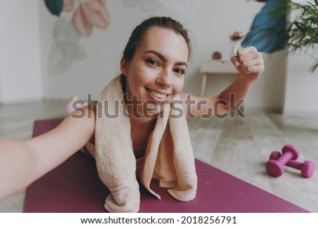 Full body close up fun young sporty athletic fitness trainer instructor woman in pink tracksuit towel do selfie shot mobile cell phone show muscles do yoga exercises lying on mat floor at home indoor