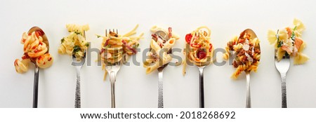 Top view of forks and spoons with different types of yummy pasta placed in row on gray background