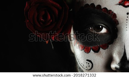 Mexican day of the dead. Young woman with sugar skull Halloween makeup looks at the camera with one eye. Extreme close-up. Happy Halloween. 