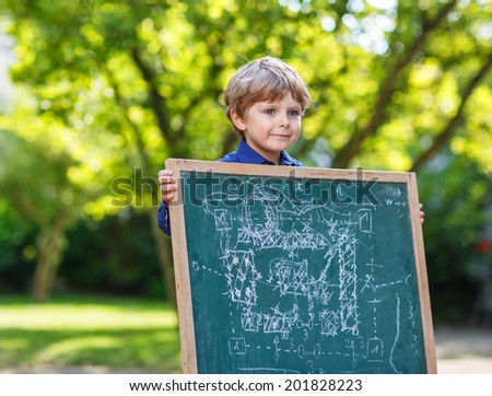 Little pupil boy at blackboard making project presentation, outdoor school or nursery. Back to school concept.