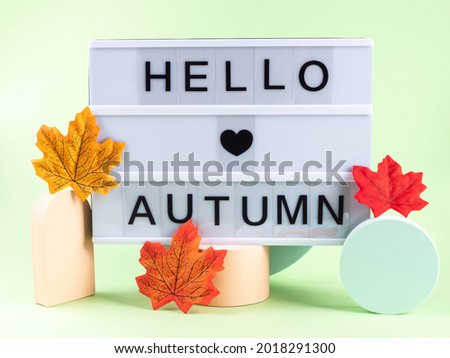 Hello autumn text on lightbox with fall leaves on green and orange podiums. Trendy modern geometric seasonal poster