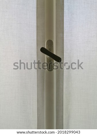 Handle on a closed window frame with white curtains.