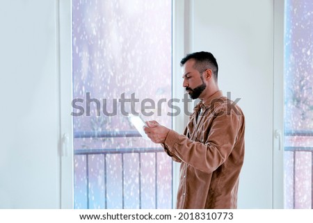 Handsome Man using tablet computer by the Window with snow falling outside.  Using new application on digital device