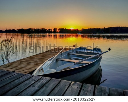 Photo of an empty boat at the pier in the lake at sunset in summer
