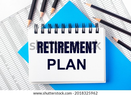 White notebook with the text RETIREMENT PLAN on the table next to black pencils on a blue background and reports. Business concept