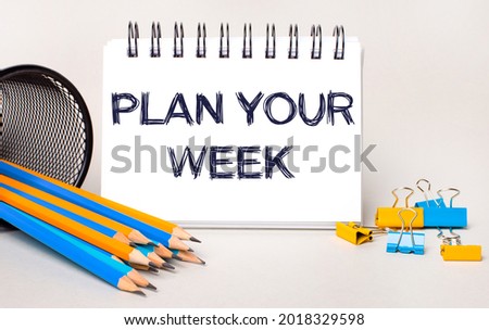On a light background, yellow and blue pencils and paper clips and a white notebook with the text PLAN YOUR WEEK