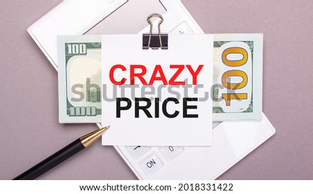 On a gray background, there is a white calculator, a pen, cash, and a piece of paper under a black paper clip that says CRAZY PRICE. Business concept