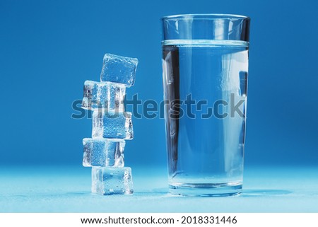 A glass of ice and clear water, ice cubes on a blue background.