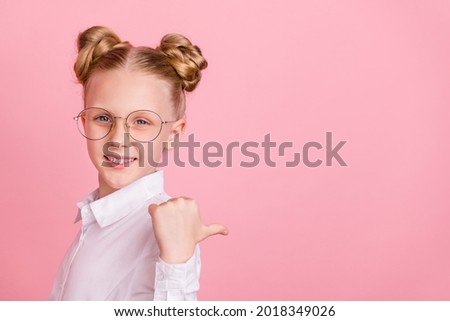 Profile photo of funny little girl point empty space wear white shirt spectacles isolated on pastel pink background