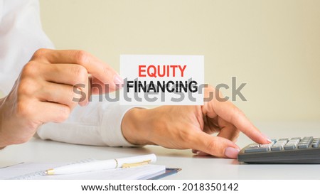 equity financing, message on business card shown by woman pressing calculator key at workplace in light office, selective focus, business and financial concept