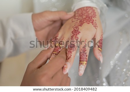 The groom puts a wedding ring on the bride's finger decorated with henna