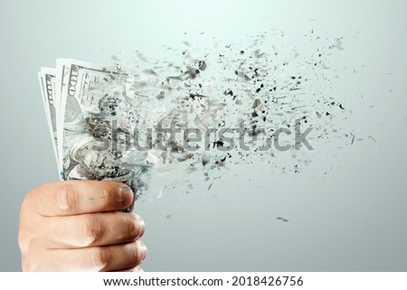 A hand holds a hundred dollar bills that dissolve into thin air. The concept of big expenses, loans, mortgages, big purchases