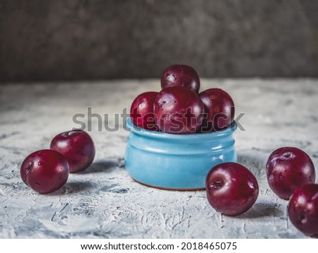 Red plums in a blue clay vase on a light background