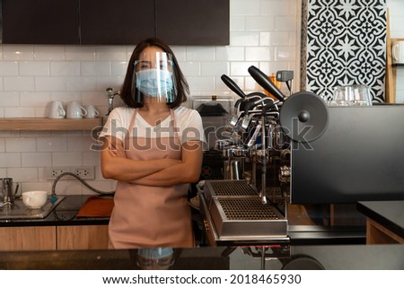 Portrait of a happy woman Asian waitress wearing a face mask and  standing at a coffee shop, Small business owner and startup with a cafe shop concept