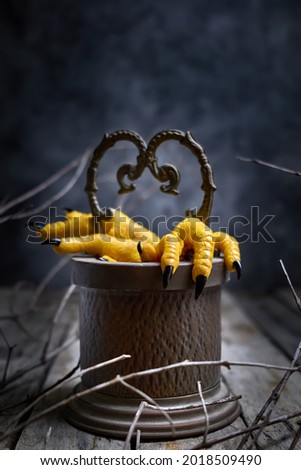 Halloween concept.Two Hen's paws with long nails manicured with black nail polish climb out of the well  on old wooden table on black background with fog and smoke.