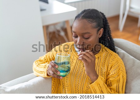 Concept of suffering from terrible pain. Beautiful, sad, upset, unhappy, troubled, weak woman with black hair, wearing casual clothes is sitting on a sofa and taking a pill