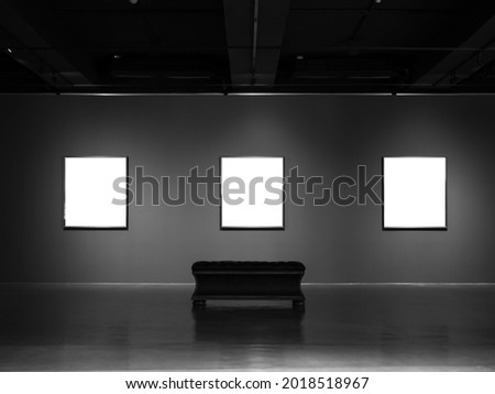 Three mockup white blank museum art frames on dark grey wall background with lighting and empty museum seating bench.