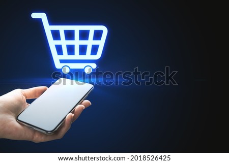 Close up of woman hands holding phone with abstract shopping cart on blue background with mock up place. E-commerce and online shopping concept