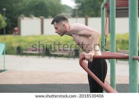 Attractive Caucasian young brunette man in sportswear doing push-ups on the bars at a playground on a warm summer day. Sports, workout, health, body care. Royalty-Free Stock Photo #2018530406