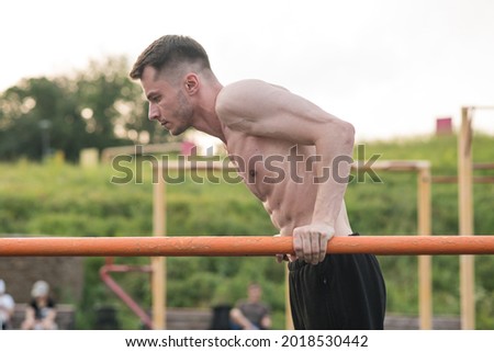 Attractive Caucasian young brunette man in sportswear doing push-ups on the bars at a playground on a warm summer day. Sports, workout, health, body care. Royalty-Free Stock Photo #2018530442