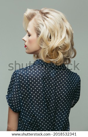 Beautiful blonde. Portrait of young woman in retro style, fashion of 70s, 80s years isolated on gray background. Concept of emotions, beauty. Female model in vintage outfits. Back view