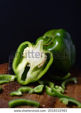 Vibrant green bell peppers cut and whole placed on a wooden board