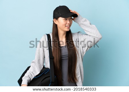 Young sport Chinese  woman with sport bag over isolated blue background smiling a lot