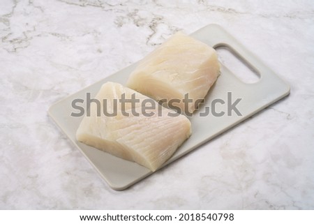 Raw fresh two pieces of halibut fish fillet on cutting board on white or grey background close up and isolated, seafood prepared for cooking
