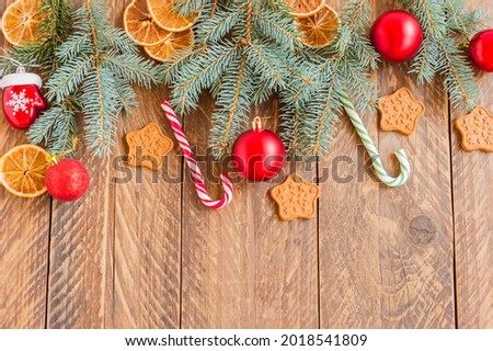 Christmas fir-tree branches with baubles, candy canes, dry oranges and star shape cookies on wooden background with copy space.