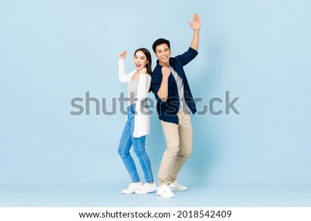 Full length portrait of cheerful Asian couple standing back to back smiling and clenching fists in light blue isolated studio background Royalty-Free Stock Photo #2018542409