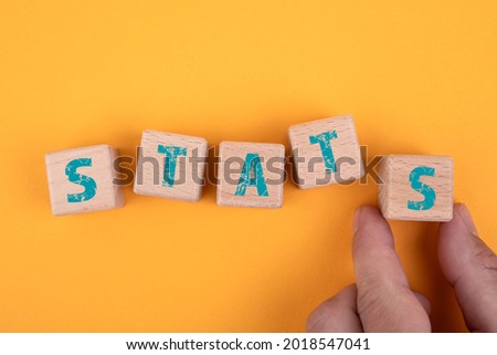 STATS. Wooden blocks and a man's hand on a yellow background.