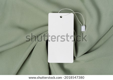 White clothing tag, label blank mockup template with the ribbon, to place your design. On a premium cotton green khaki fabric textile background.