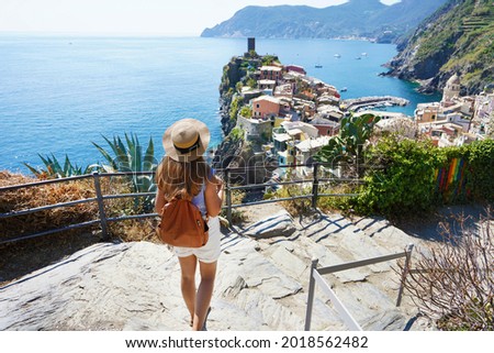 Tourism in Italy. Young female backpacker going downstairs in the Cinque Terre National Park. Beautiful girl walks the Azure Trail and looking at Vernazza town, Italy. Royalty-Free Stock Photo #2018562482