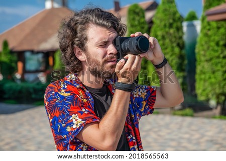 A man with a beard leads a shot of a professional camera outdoors in the summer