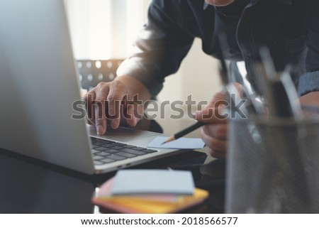 Business man planning new startup project on notepad, writing with pencil on reminder note paper with laptop computer, business document on table in modern office, close up. Business process concept