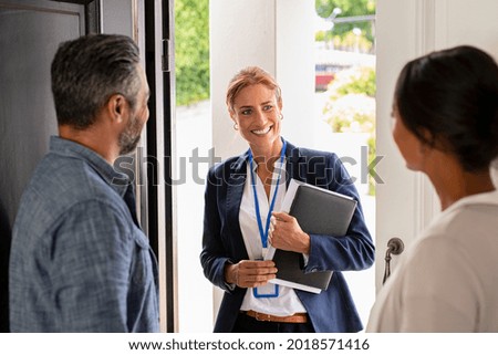 Smiling mature social counselor meeting mature couple at home. Happy multiethnic man and latin woman greeting agent at home standing near door. Successful social worker consultant on the doorstep. Royalty-Free Stock Photo #2018571416