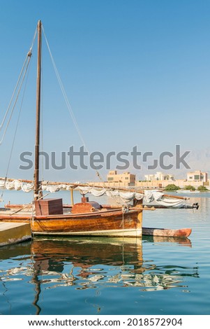 view to traditional fishing boat in harbour with calm water and reflections under blue sky in UAE