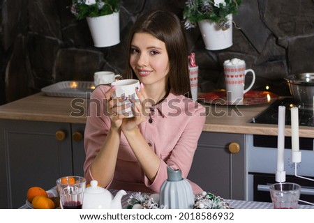 Christmas, happy woman in a dress in the kitchen drinks tea with sweets and tangerines.