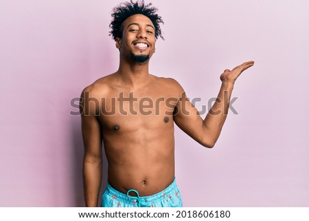 Young african american man with beard wearing swimsuit smiling cheerful presenting and pointing with palm of hand looking at the camera. 