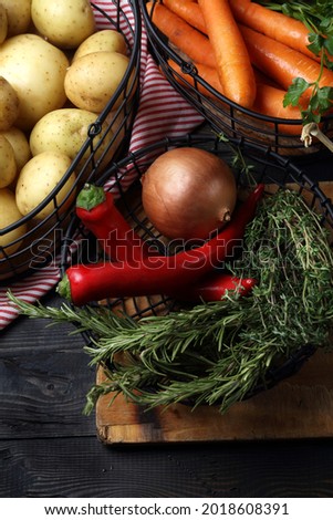 Raw potatoes, carrots, onion, garlic, chili peppers, thyme, rosemary and parsley in metal baskets on the table